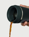 Hand pouring coffee from Hedoniq charcoal (black) travel cup by TOPL, designed for spill-proof convenience.