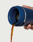 Hand pouring coffee from Hedoniq navy travel cup by TOPL, designed for spill-proof convenience.