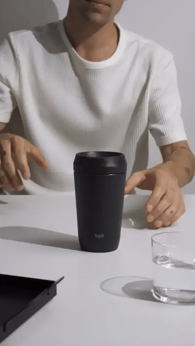 Hand demonstrating the Hedoniq TOPL reusable flask in black, showing the secure spill-proof lid.