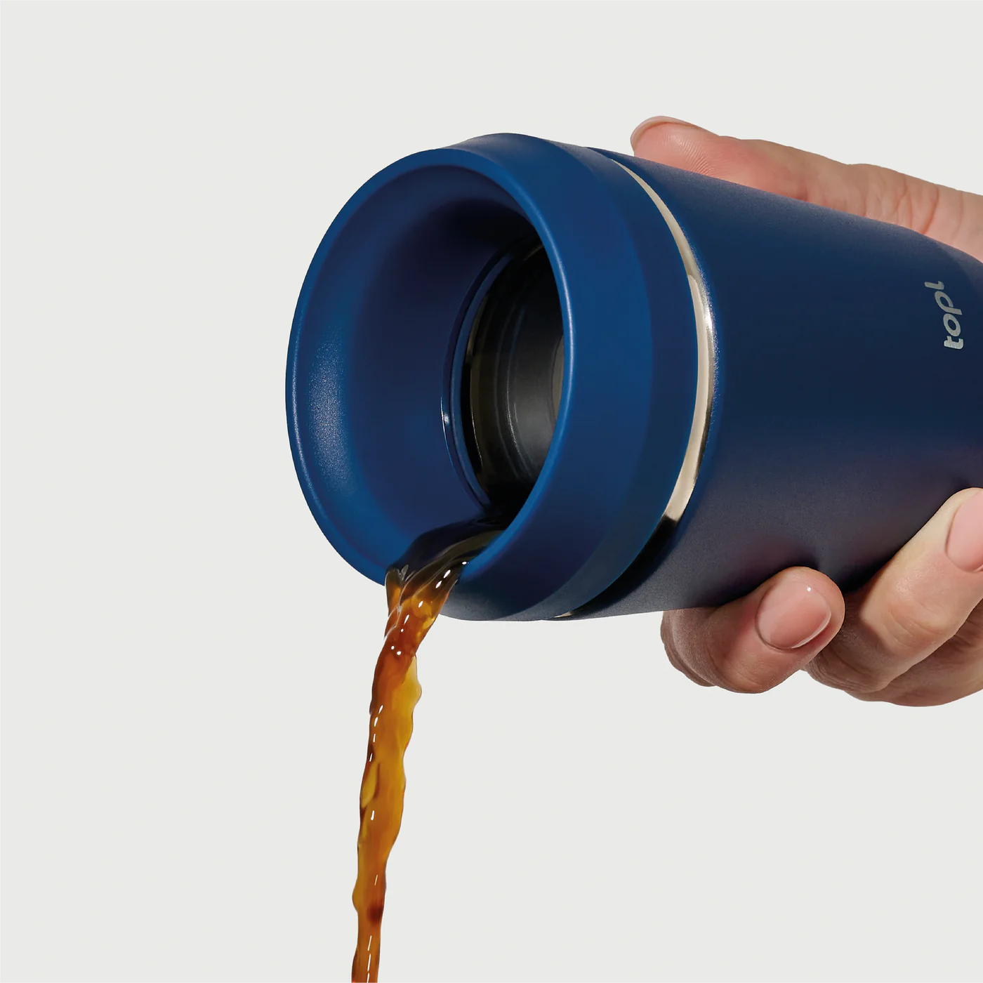 Hand pouring coffee from Hedoniq navy travel cup by TOPL, designed for spill-proof convenience.