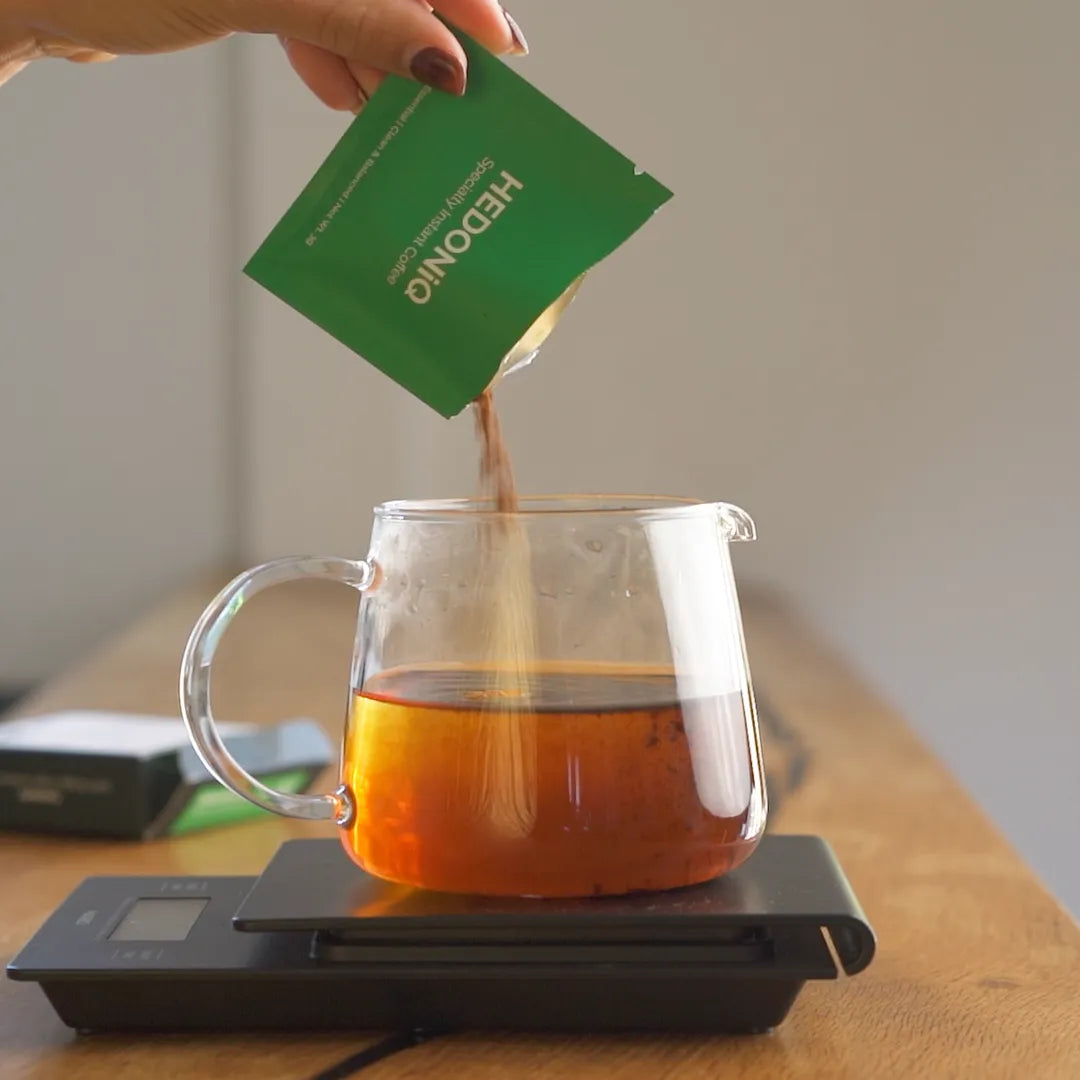 Brewing Hedoniq Essential Box specialty instant coffee in a jug on scales and pouring into two cups in a home kitchen.
